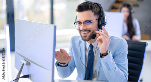 Successful businessman call center operator in suit talking with customer, surrounded by technology and other agents at office.