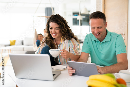 Happy young married couple enjoying their time while surfing the net on laptops and drinking coffee.