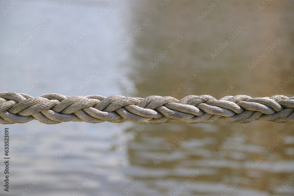Closeup of a braided rope using as a mooring line against a calm water Closeup of a braided rope using as a mooring line against a calm water