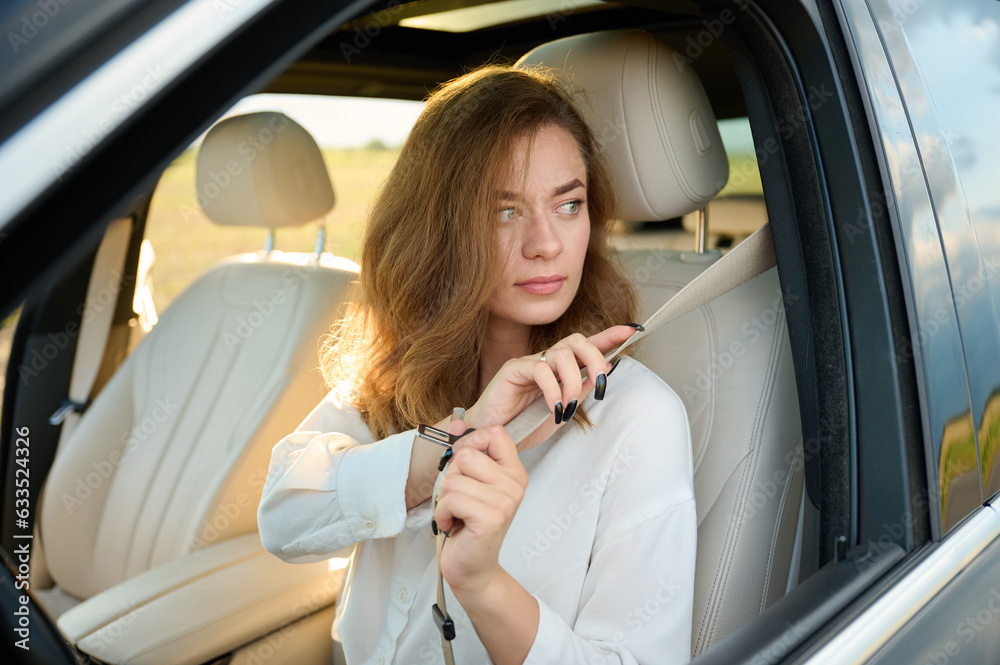 Pretty business lady fastens seat belt in new modern technological car. Happy woman fastening her seatbelt while sitting at the steering wheel of her car. Buckle up and drive safe. Pretty business lady fastens seat belt in new modern technological car. Happy woman fastening her seatbelt while sitting at the steering wheel of her car. Buckle up and drive safe.