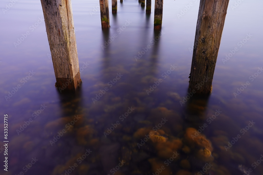 Symmetrical wooden poles in water that reflects purple sky.