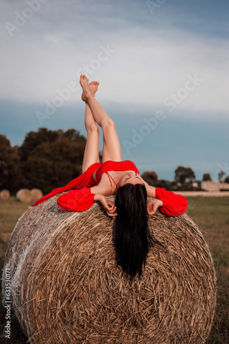 A young woman lies on a stack of straw in a field. Summer outdoor recreation