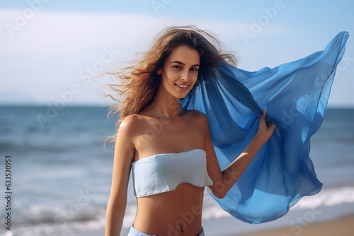 Attractive young woman waving blue scarf in wind at beach.