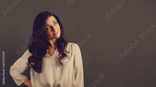 Beautiful happy smiling woman with long brown curly healthy hair looking up and dreaming about in white shirt, formal clothing. Closeup studio toned portrait photo