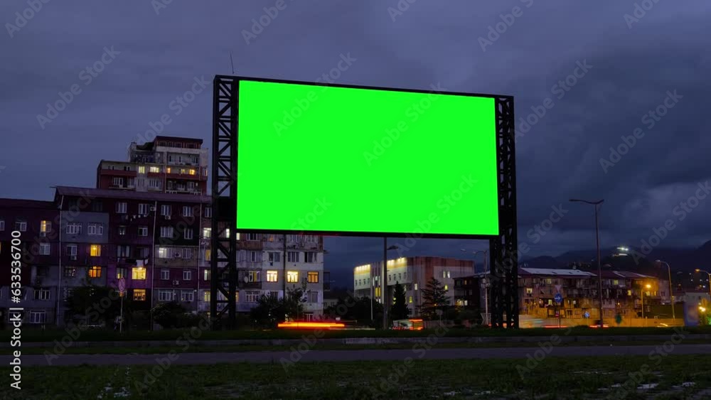 Timelapse: blank green billboard, large display, fast moving car traffic in evening time with warm night illumination, gets dark. Green screen, time lapse, template, mock up and copy space concept