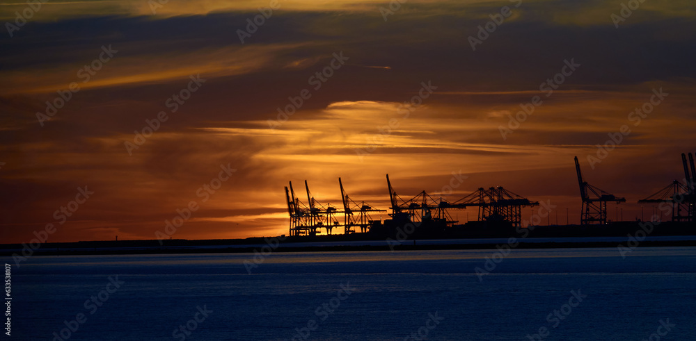 Le Havre port cranes back-lit by orange sky and clouds of a distant sunset