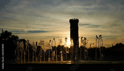 Small vertical water jets in front of a sunset and an old tower in an urban environment © Sylvain