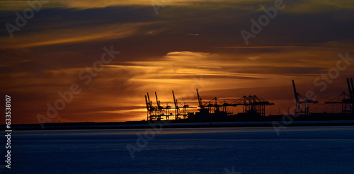 Le Havre port cranes back-lit by orange sky and clouds of a distant sunset © Sylvain