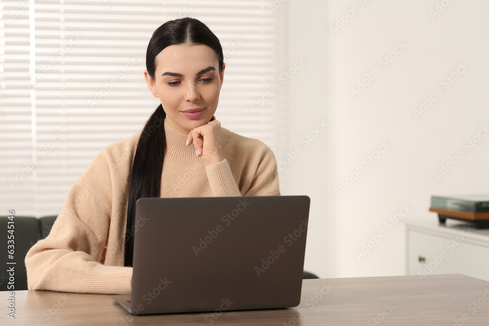 Woman working with laptop at wooden desk in room
