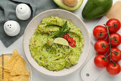 Delicious guacamole with nachos chips and ingredients on white table, flat lay