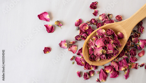 Fototapeta Naklejka Na Ścianę i Meble -  Dried rose petals in a wooden spoon, top view. Light background, copy space. Pink colored organic herb used for perfumes, cosmetics, teas and baths.