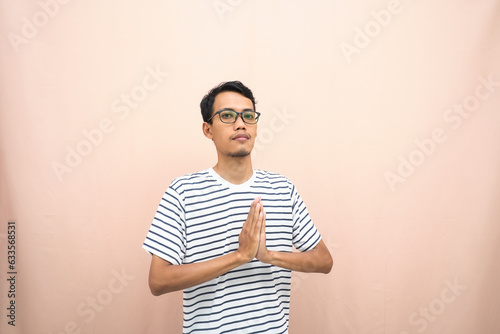 Asian man in glasses wearing casual striped t-shirt, greeting pose and smiling. Isolated beige background.