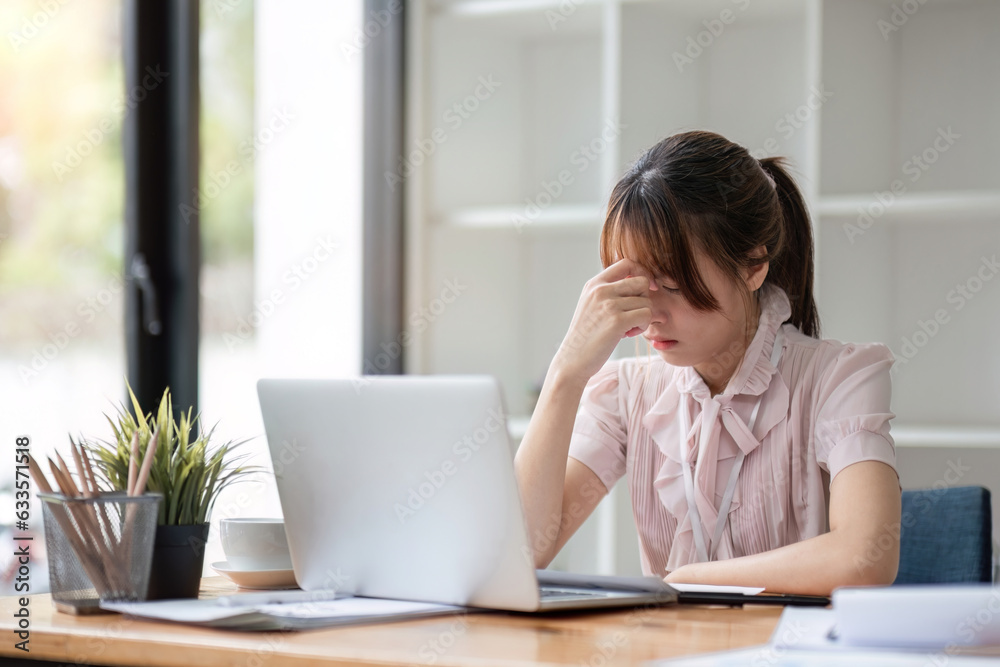 Portrait image of Young Asian businesswoman bowing and holding her head stressed expression with financial documents on working table.