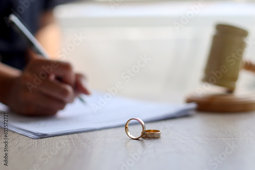 Wedding rings on wooden table with hand signing documents and judge gavel on the background. Marriage and divorce concept photo