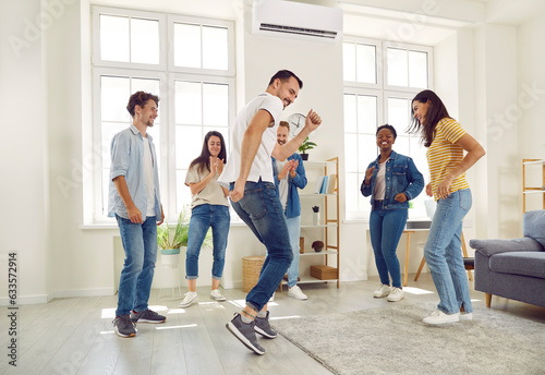 Six cheerful best friends are dancing and fooling around listening to their favorite track at home party. Multiracial men and women laughing and having fun standing in circle in living room.
