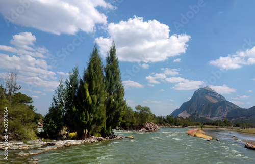 Bright blue sky white clouds, wide rapids river and mountains, pine spruce forest and rocks on river bank, scenic landscape, nature wallpaper, background or backdrop