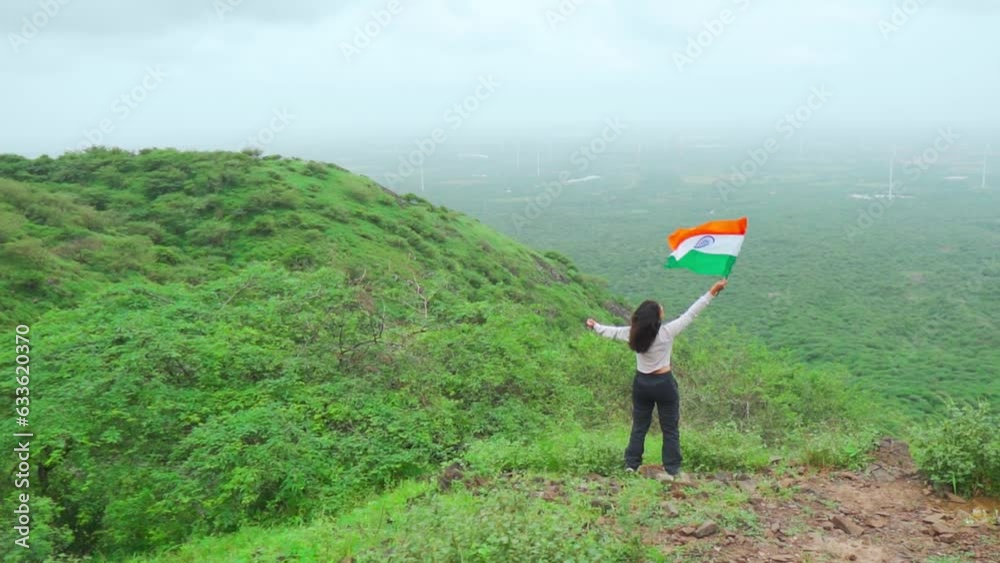 Indian girl waving Indian flag while standing on top of the mountain at Nanamo Hill, Kutch, India. People celebrating republic day outdoors. Female waving flag on mountain summit. Indian girl waving Indian flag while standing on top of the mountain at Nanamo Hill, Kutch, India. People celebrating republic day outdoors. Female waving flag on mountain summit.