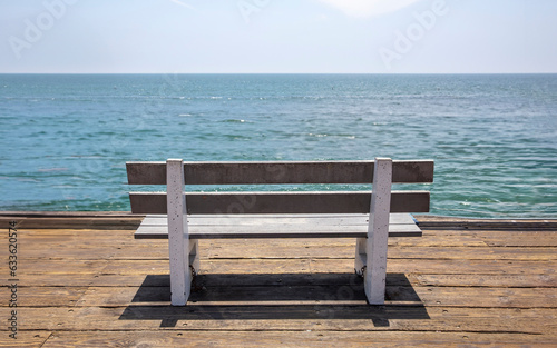 Empty wooden park bench on waterfront wood platform. Sunny day, calm sea, blue sky background. USA © Rawf8
