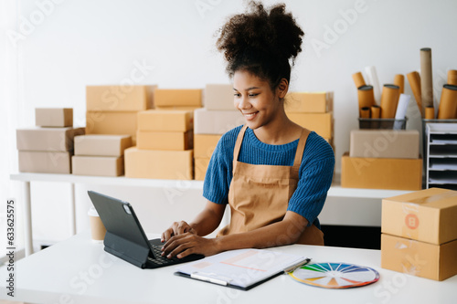Startup small business SME, Entrepreneur owner African woman using smartphone or tablet taking receive and checking online purchase shopping order to preparing pack product box. in office.