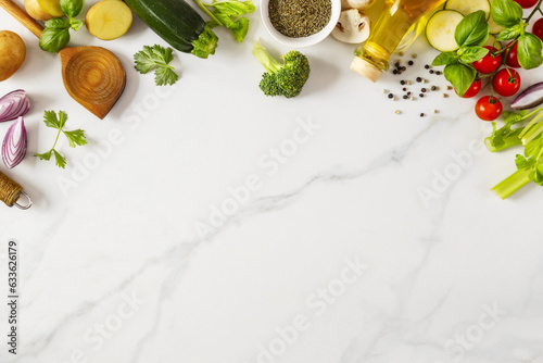 Food cooking ingredients background with fresh vegetables, herbs, spices and olive oil on marble table with copy space top view. Healthy vegetarian eating
