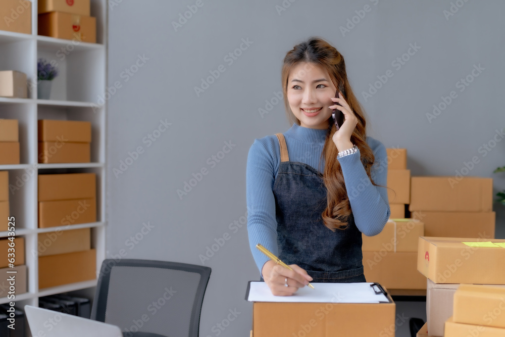 Happy Asian woman owner talking on the phone with customers, taking orders and preparing delivery. Happy Asian woman owner talking on the phone with customers, taking orders and preparing delivery.