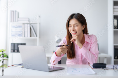 Smiling young happy Asian businesswoman working with laptop and documents in office. Accountant or beautiful asian female worker working happily in the office.