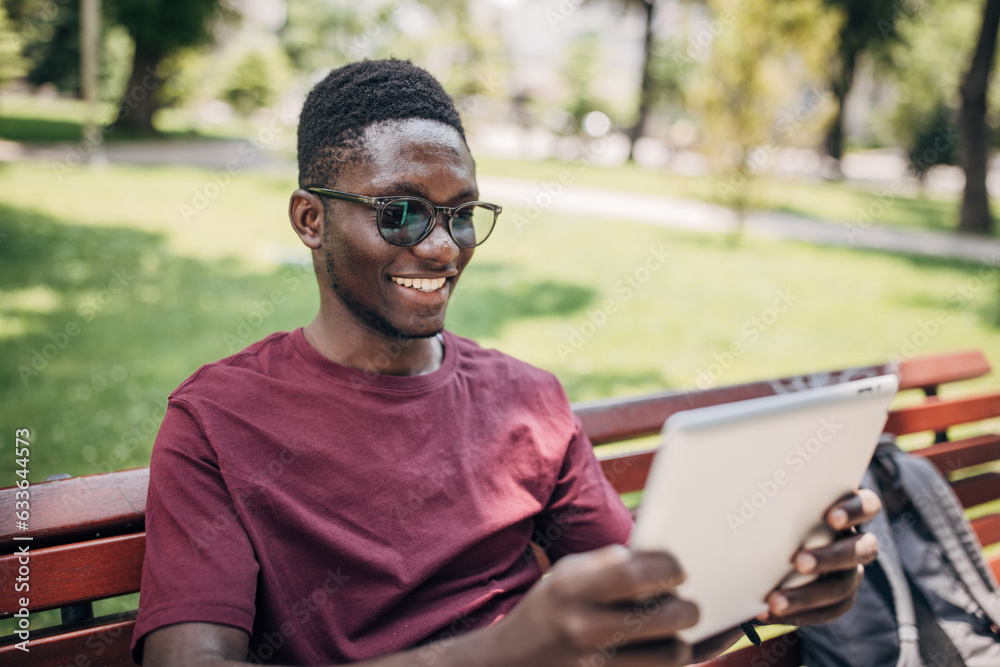 Fototapeta premium Young man sitting in the park relaxing in the nature and using digital tablet