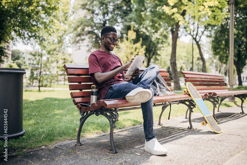 Young man sitting in the park relaxing in the nature and using digital tablet