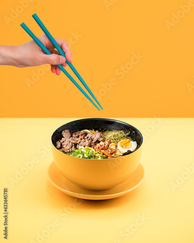 Photo of Japanese ramen soup with chopsticks and hand on the background.