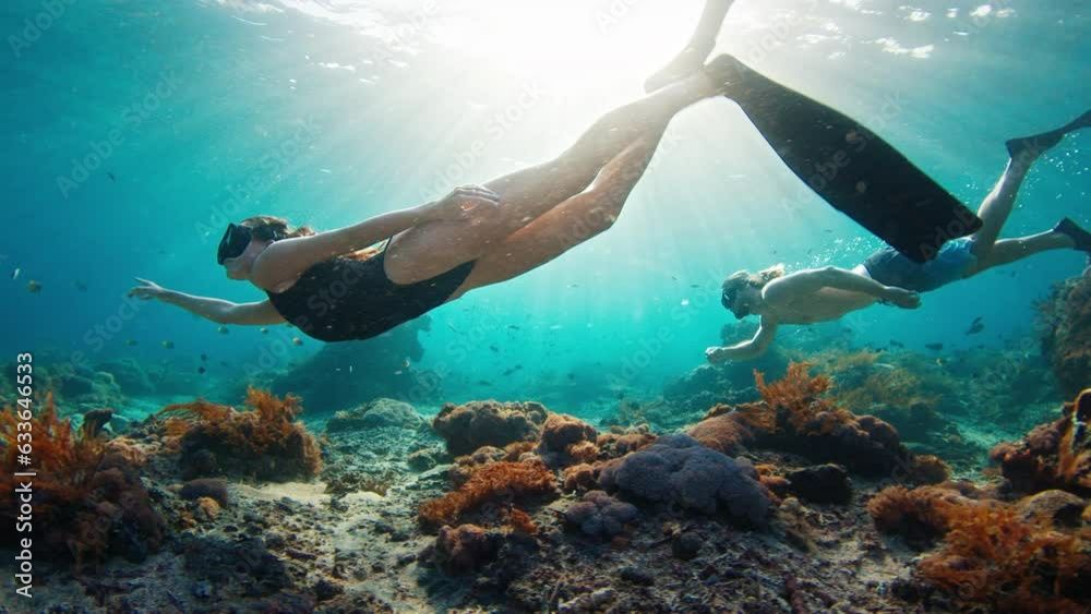 Couple freediving. Young fit freedivers man and woman swim underwater over the healthy coral reef near the island of Nusa Penida in Bali, Indonesia