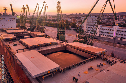 Aerial of wheat loading to bulker ship cargo hold at sea grain elevator in sea port at sunset. Black Sea Grain Initiative and grain deal