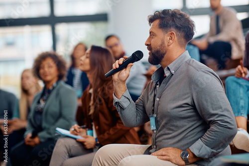 Business seminar attendee talking on microphone while sitting in audience at convention center.