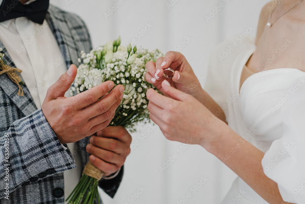 Engagement closeup. Marriage. Newlyweds stands on wedding ceremony under arch decorated white flowers. Bride and groom getting married and wear wedding rings. Woman and man while ceremony. Vows