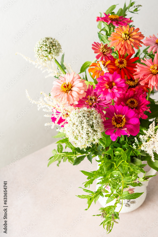 Obraz premium Summer bouquet of colorful Zinnia, onion inflorescences and mint sprigs, bouquet of flowers on the table near the wall, home decoration with flowers
