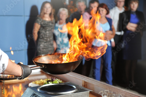 Cooking show for people, chef cooks, fries meat in a frying pan with fire