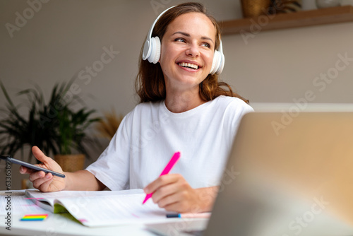 Young female university  student listens to educational audio records using her wireless headphones and her smart phone.