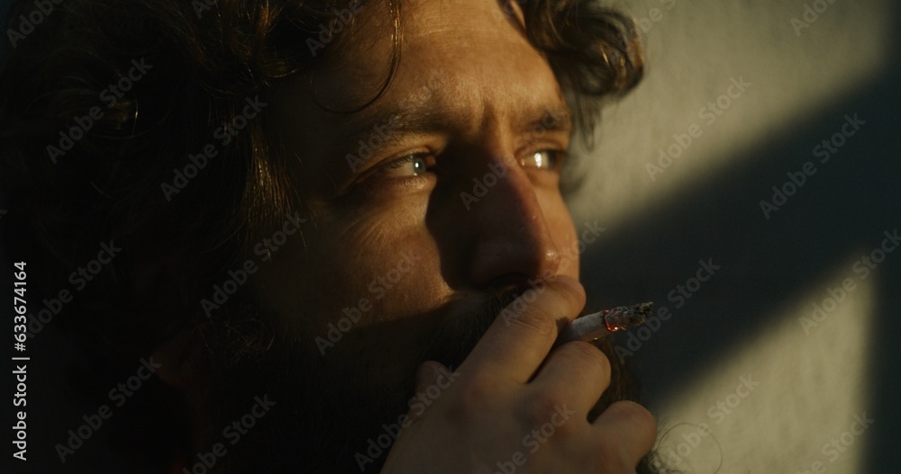 Obraz premium Depressed prisoner in orange uniform sits in prison cell, smokes cigarette. Criminal, inmate serves imprisonment term for crime in jail. Detention center or correctional facility. Close up. Portrait.