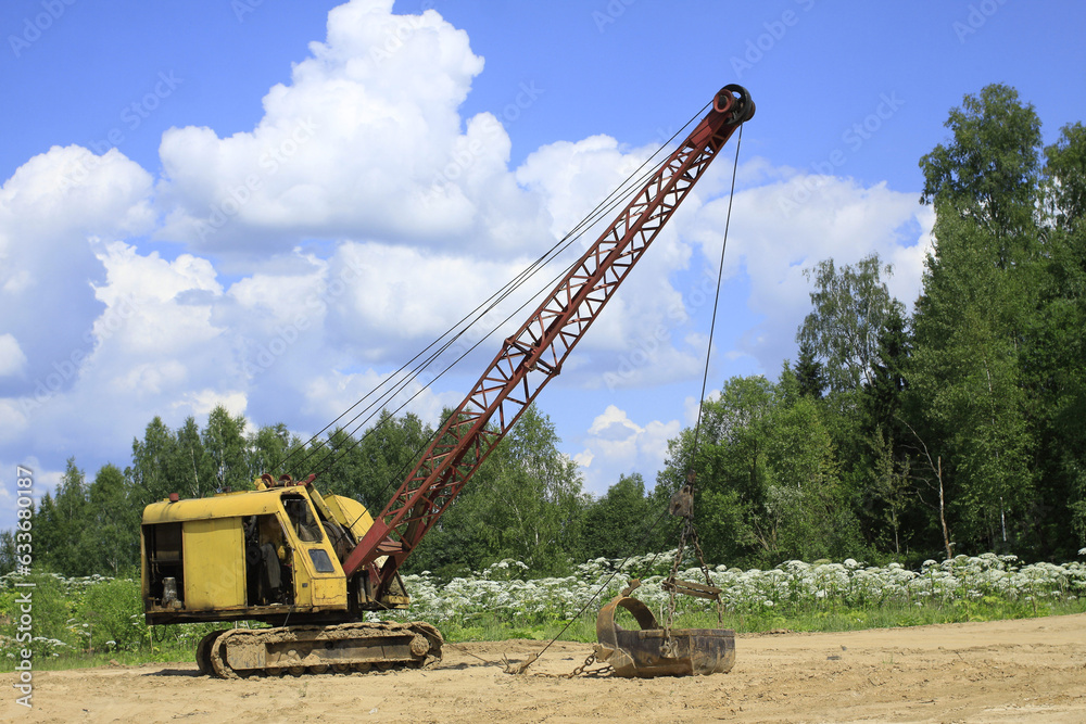 Yellow excavator with long boom stands on the forest edge in sunny day side view Yellow excavator with long boom stands on the forest edge in sunny day side view