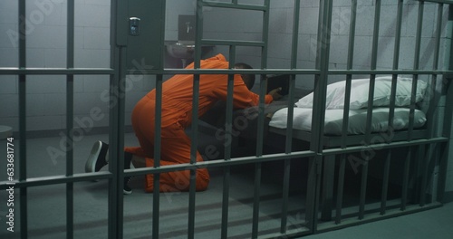 Canvastavla Religious African American prisoner in orange uniform kneels near the bed, prays to God in prison cell holding Bible