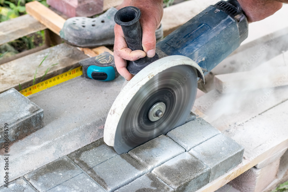 A worker on the street cuts paving slabs with a grinder for further paving on a sunny summer day