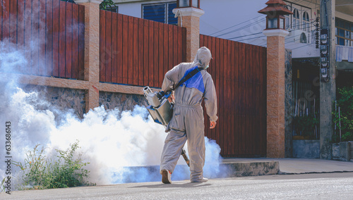 Rear view of healthcare worker in protective clothing using fogging machine spraying chemical to eliminate mosquitoes and prevent dengue fever on street in public community area photo