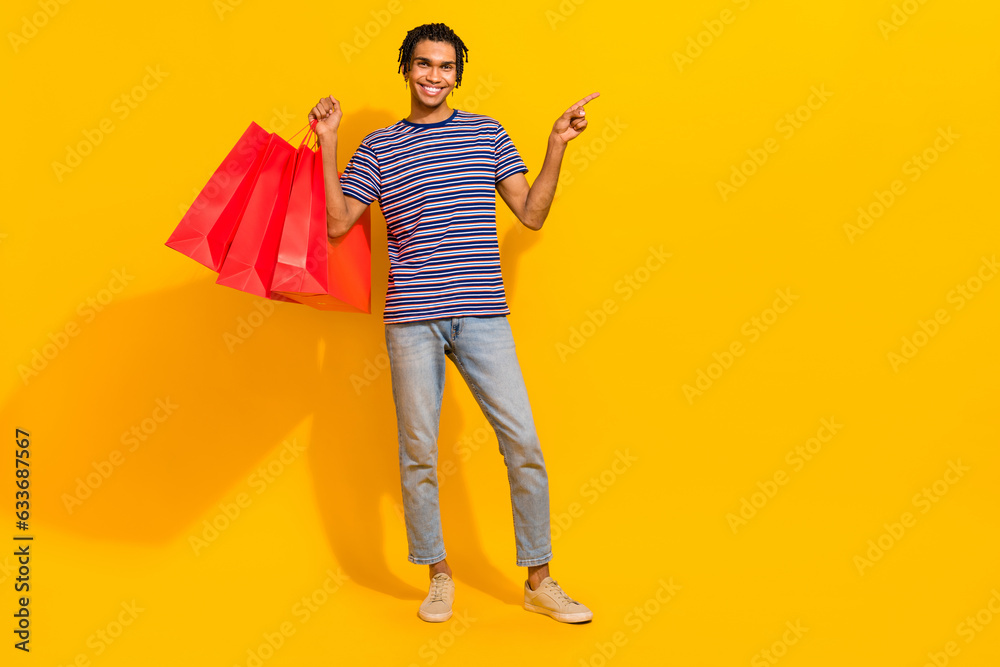 Fototapeta premium Full body portrait of positive nice man hold store bags indicate finger empty space isolated on yellow color background