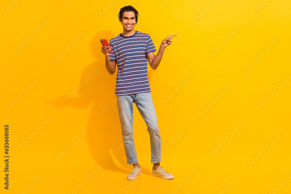 Full body photo of handsome man hold smart phone direct finger empty space offer ad isolated on yellow color background Full body photo of handsome man hold smart phone direct finger empty space offer ad isolated on yellow color background