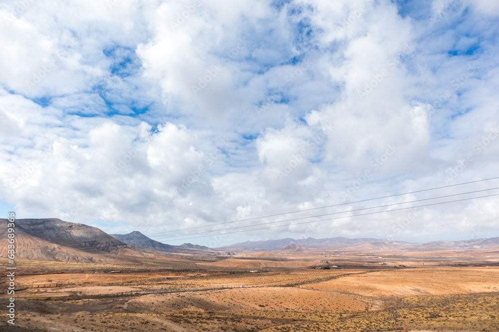 Fototapeta premium Desertic landscape of the interior of Fuerteventura island. Rocky hills with white sand. Sky with big white clouds. Sunny day Fuerteventura, Canary Islands, Spain.