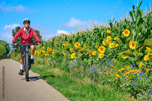 nice senior woman cycling with her electric mountain bike in a blooming sunflower field