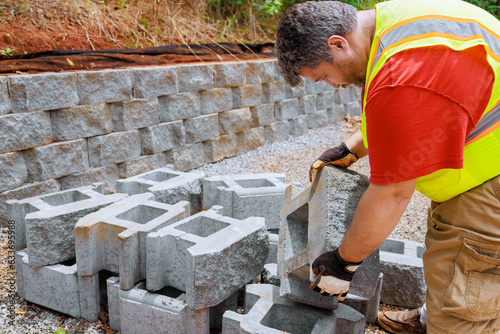 Construction worker lifts concrete block and places it on retaining wall