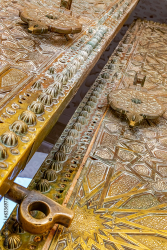 Huge door ajar with islamic andalusian 3D engravings and sculptures in Sidi Boumediene mosque of Tlemcen city in Algeria. A low angle view with metallic latch and handle and feature geometric patterns photo