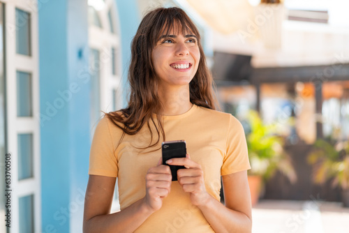 Young woman at outdoors using mobile phone and looking up