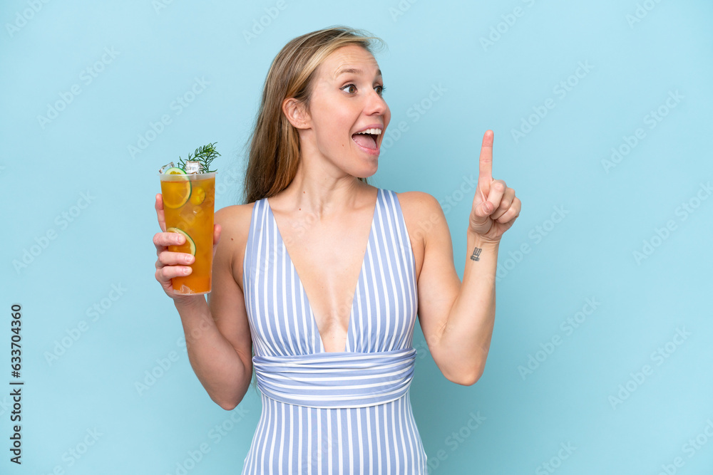 Young blonde woman wearing swimsuit holding a cocktail isolated on blue background intending to realizes the solution while lifting a finger up Young blonde woman wearing swimsuit holding a cocktail isolated on blue background intending to realizes the solution while lifting a finger up