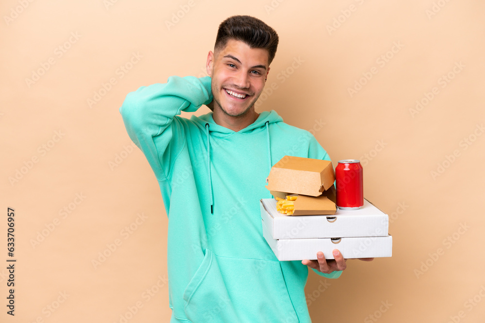 Young caucasian man holding fast food isolated on beige background laughing Young caucasian man holding fast food isolated on beige background laughing
